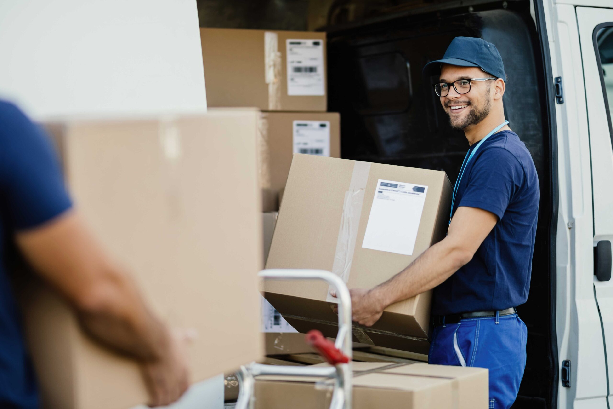 young-happy-manual-worker-carrying-cardboard-boxes-delivery-van-while-communicating-with-his-colleagues